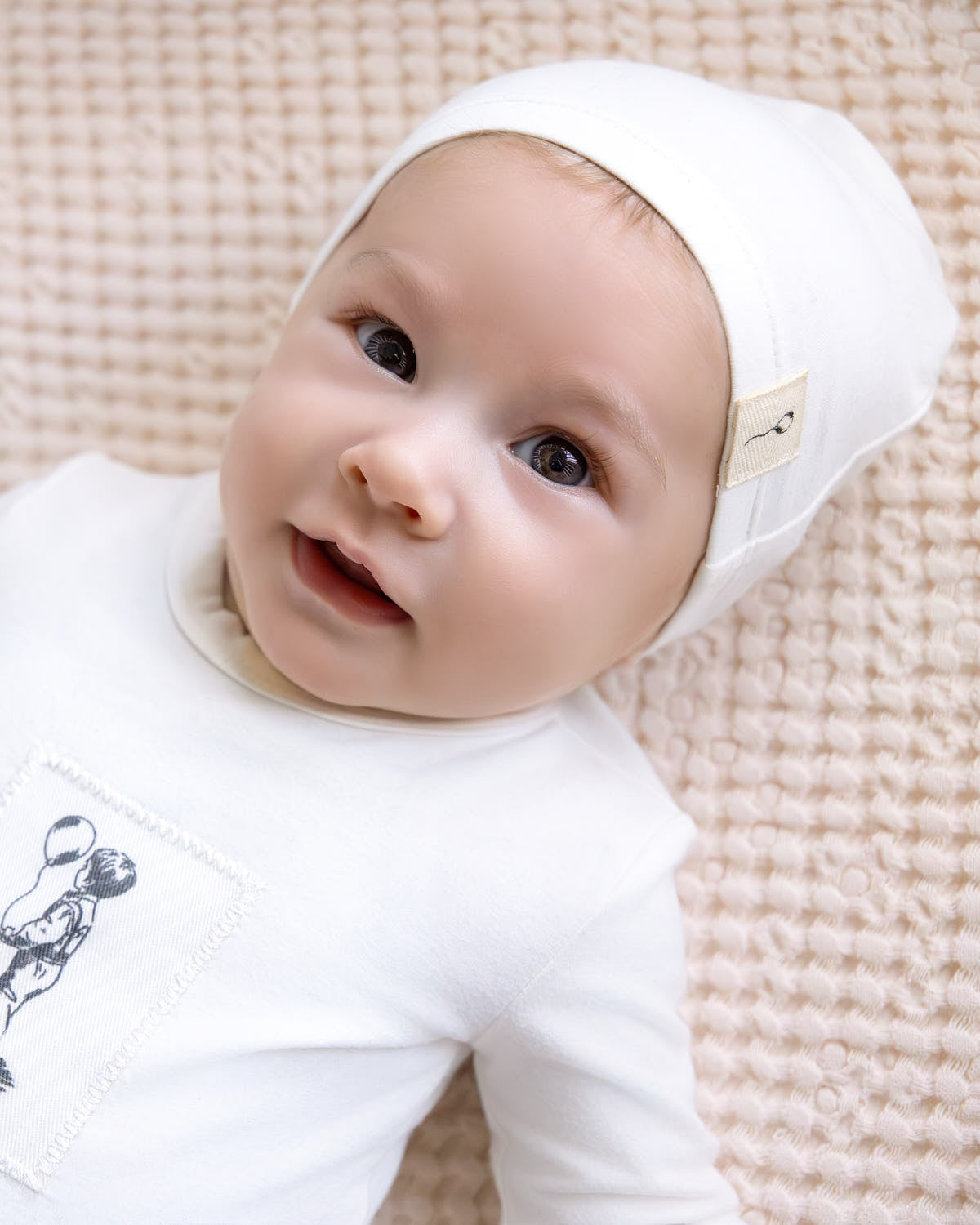 Baby wearing a white hooded outfit with a soft textured background