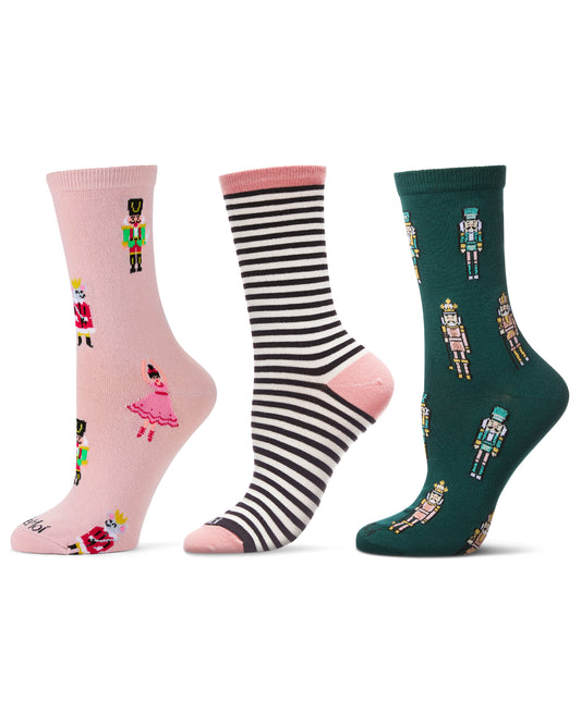 Three pairs of crew socks displayed side by side on a white background: one light pink with nutcracker and ballerina illustrations, one black and white striped with pink toe/heel areas, and one dark green with nutcracker illustrations.