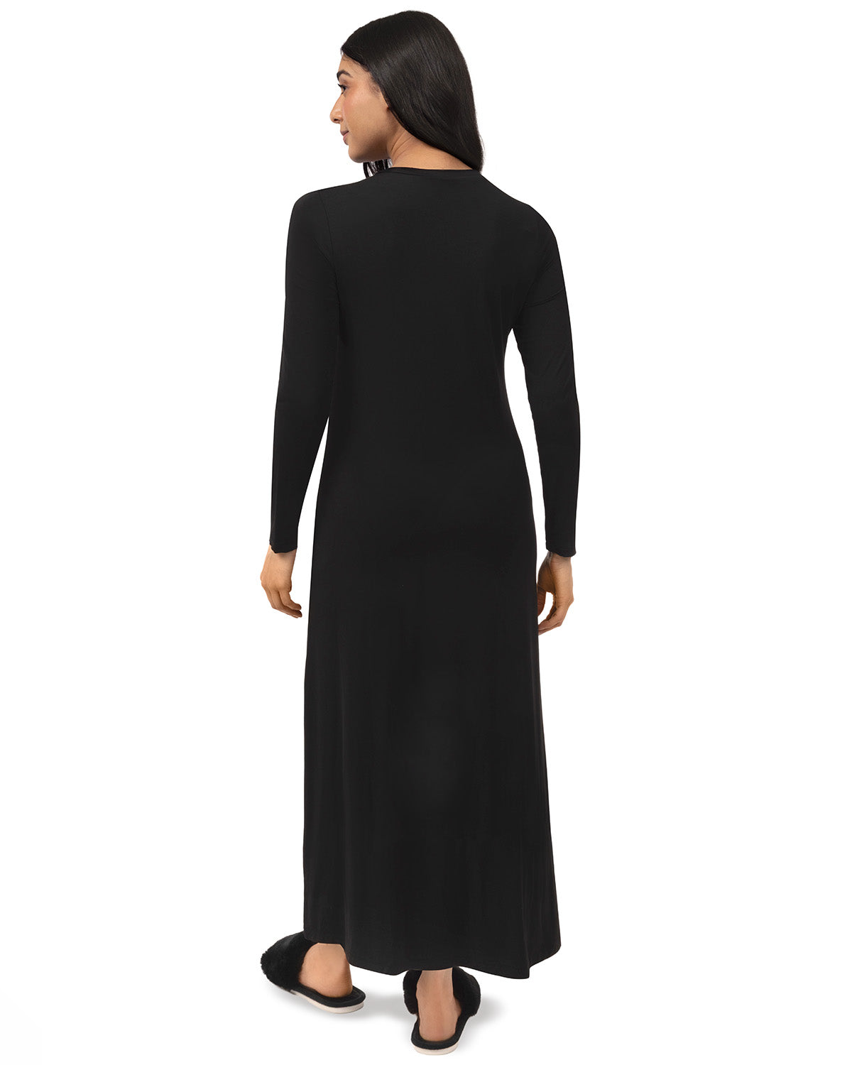A woman shown from the back wearing a long-sleeve black maxi dress and black flat shoes against a plain white background.