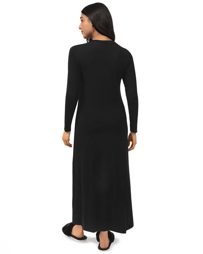 A woman shown from the back wearing a long-sleeve black maxi dress and black flat shoes against a plain white background.