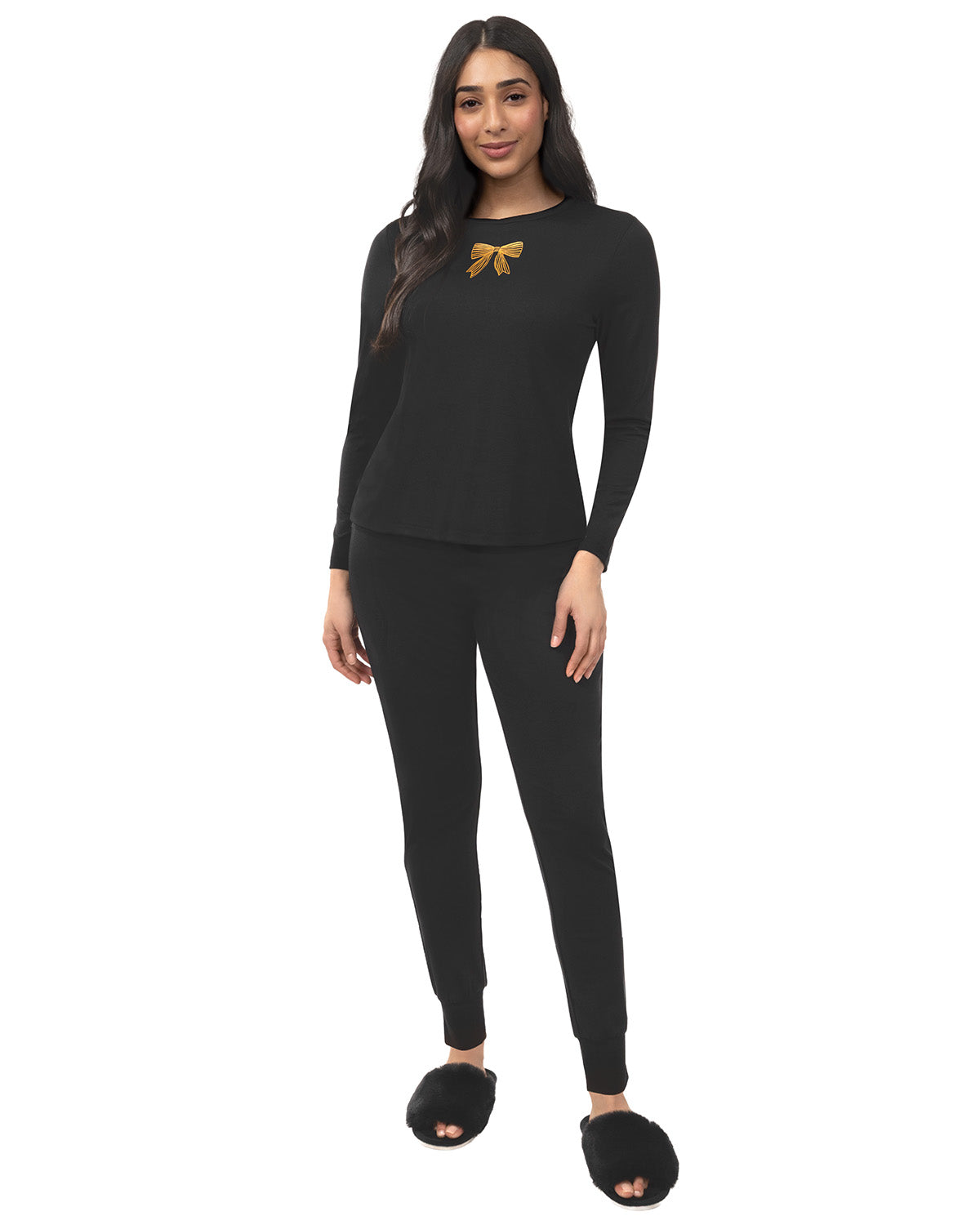 A woman modeling a black long-sleeve top and matching black pants set, featuring a small gold bow graphic on the chest, against a plain white background.