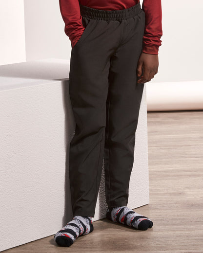 A person wearing dark charcoal gray jogger-style pants with an elastic waistband, paired with a red long-sleeve top and patterned socks, standing next to a white block on a light wood floor.