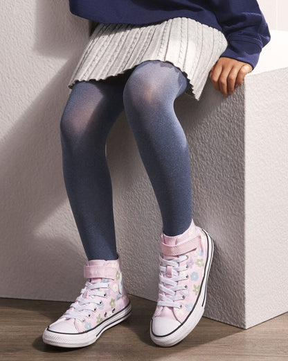A child wearing blue-gray tights, a white pleated skirt, a navy top, and pink floral high-top sneakers, seated on a textured white block.