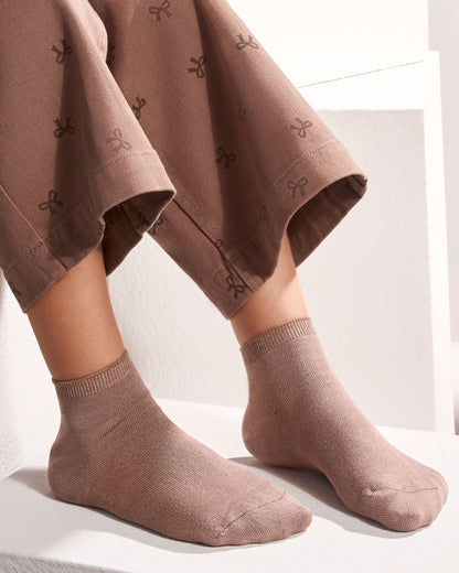 A close-up of a person's feet wearing taupe-brown ankle socks with a matching patterned trouser leg, sitting on a white step.